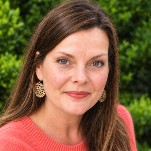 A head and shoulders portrait photo of Juliette Willett, a white female with long straight hair, wearing a red jumper and smiling at the camera.