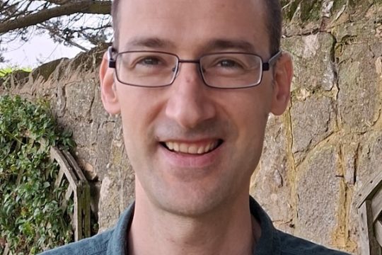 A head and shoulders photo of Simon Casciano wearing glasses and standing in a garden