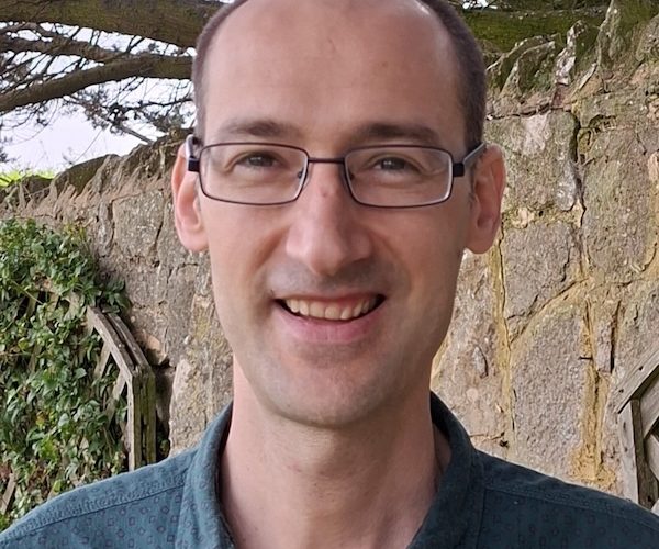 A head and shoulders photo of Simon Casciano wearing glasses and standing in a garden